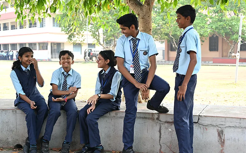 Don Bosco students in uniform chatting on a low wall beside the school ground
