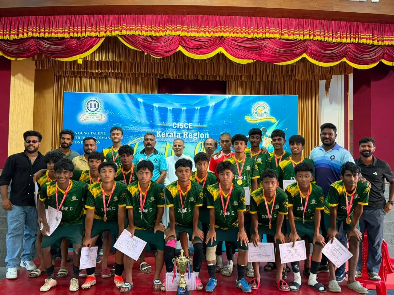 The Don Bosco U-17 boys football team with medals and certificates on stage after winning the C Zone title